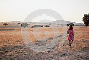 Women ia a red flower dress walking on a Cork Oak field near a dirt road