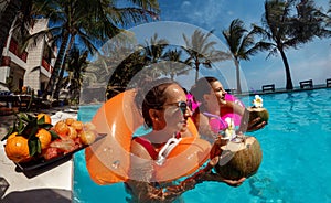 Women in inflatable ring relaxing with cocktail at the swimming pool outdoors
