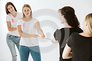 Women in jeans and t-shirts with pink bows pulling the rope in white empty interior