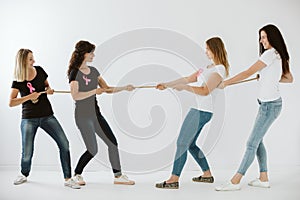 Women in jeans and t-shirts with pink bows pulling the rope in white empty interior