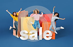 Women jumping near large bags and word sale, blue background