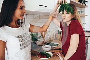 Women in the kitchen joke, laugh and have fun. Playing with vegetables