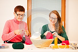 Women knitting with red wool. Eldery woman transfering her knowledge of knitting on a younger woman on handcraft workshop.