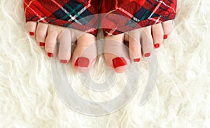 Women leg with red pedicure on white warm plaid