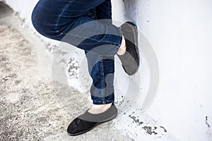 Women legs or female legs shod in black colored shoes and blue colored jeans.