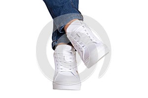 Women legs in jeans and sneakers. Woman legs in blue denim pants wearing modern white sneaker. Fashionable white footwear. Macro