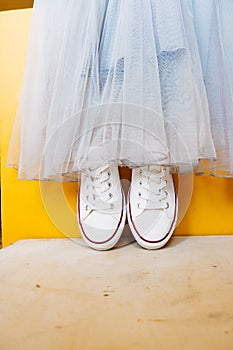 Women legs in white clean new sneakers, transparent thin socks with silver shiny stars and blue jeans on yellow background.