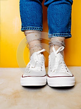 Women legs in white clean new sneakers, transparent thin socks with silver shiny stars and blue jeans on yellow background.