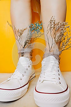 Women legs in white clean new sneakers, transparent thin socks with silver shiny stars and and dry flowers in them on yellow