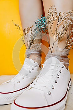 Women legs in white clean new sneakers, transparent thin socks with silver shiny stars and and dry flowers in them on yellow