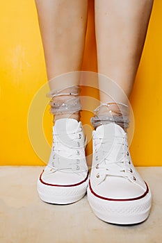 Women legs in white clean new sneakers, transparent thin socks with silver shiny stars on yellow background. combination of sports