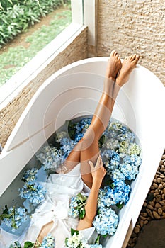 Women legsrelaxing in bath with tropical blue hydrangea.