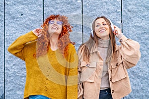 Women listening music with headphones standing in the city