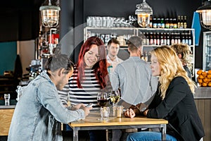 Women Looking At Friend Using Mobile Phone In Bar