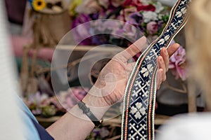 Women is looking at handmade weaved belt. Ornamental Latvian be