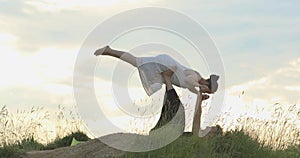 Women and man practice acroyoga near wood at sunset. Couple makes position of plane on outdoors. Background of clody sky