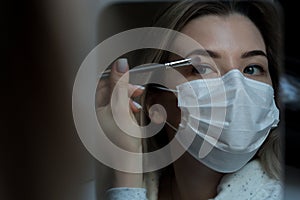 Women in a medical mask against corona virus does eye makeup