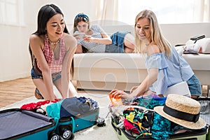 Women packing suitcases for vacation together at home, getting ready to travel concept