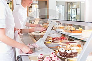 Women in pastry shop filling up sales display with pies