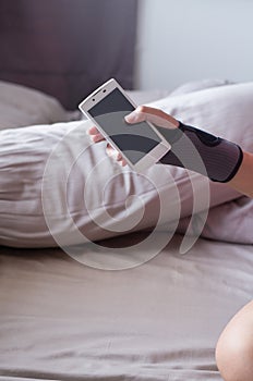 Women play mobile while elastic wrist support on hand to relieve pain