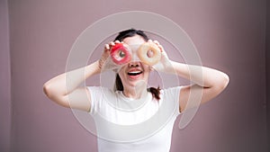 Women play with two donuts. Teens have fun with dessert. The person holding two donuts covered their faces, making is fun eyes.