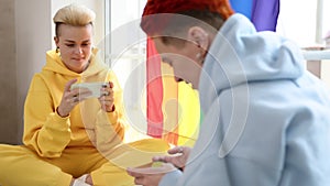 Women Playing Mobile Games Together in Cozy Modern Home with Bright Interior and Rainbow Flag