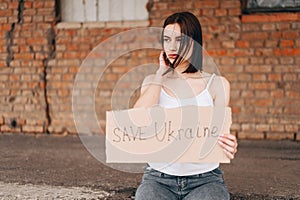 Women with Poster Save Ukraine. A woman with belligerent look looks to the side. Wind develops Hair