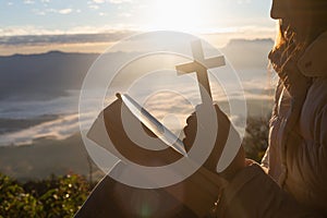 Women pray to God with the Bible and the cross on the mountain background with morning sunrise. Woman Pray for god blessing to photo