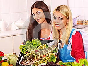 Women prepare fish in oven.