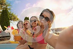 Women with refreshing drinks taking selfie at pool party