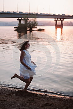 Women running along the beach at sunset. Lifestyle full-length portrait of a happy, young woman in a white dress flying