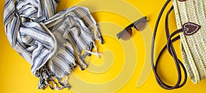 Women`s accessories for a beach holiday on a yellow background. Wicker straw bag, towel, shoes and sunglasses flat lay for a beach