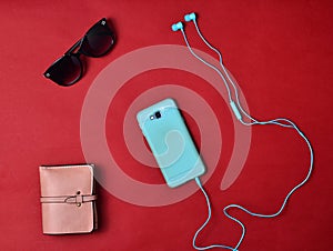 Women& x27;s accessories are lined on a red background. Smartphone, headphones, wallet, sunglasses. Flat lay