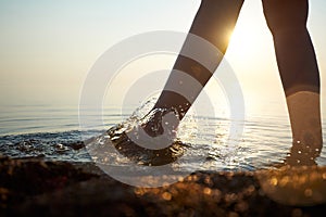 Women`s bare feet walk on water illuminated by sunlight.