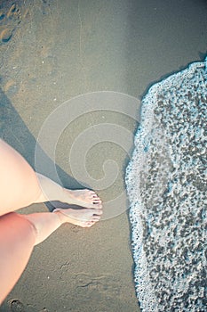 Women`s beautiful smooth legs on white sand beach