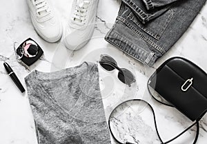 Women`s casual comfortable clothing - sneakers, jeans, pullover, crossbody bag and cosmetics on a light background, top view