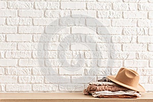 Women`s casual outfits and brown trendy hat on wooden table over white brick wall. Minimalistic concept of home decor. Template