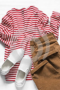 Women`s cotton t- shirt with red stripes, corduroy brown banana jeans and white sneakers on a light background, top view