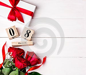 Women`s day background. 8 march wooden calendar, red roses, gift with red ribbon on the white wooden background. Copy space, flat