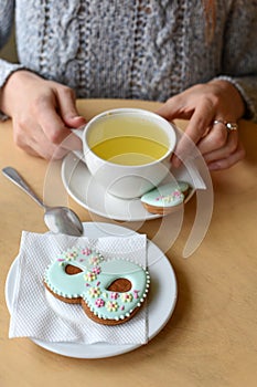 A Women`s day photo of woman`s hands, a tea pot, a cup and a cookie shaped like a figure `8`