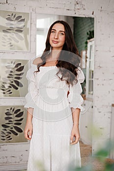 Women& x27;s day. Romantic attractive young woman 20-25 years with long curly hair in white dress is poses with crossed