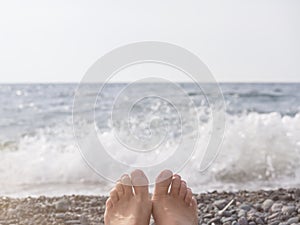 Women& x27;s feet on the background of a pebble beach and the sea