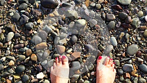 Women`s feet on the beach of the sea. Waves wash their feet, red pedicures on nails. The concept of leisure and travel