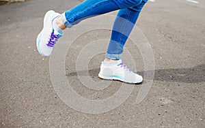 Women`s feet in blue jeans and white sneakers on the asphalt. close up