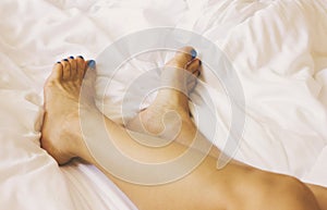 Women`s feet with blue pedicure on white bedding