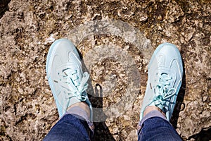 Women s feet in blue sneakers stand on a stone