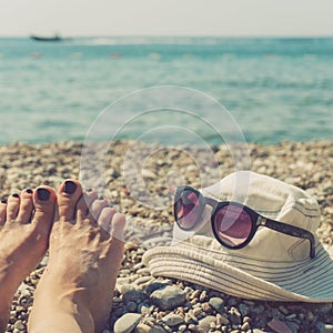 Women`s feet, cap and sunglasses on the beach
