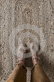 Women's feet in comfortable retro leather sandals and corduroy trousers on a jute carpet, top view