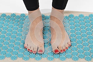 girl standing on applicators doing foot massage on a massage Mat photo