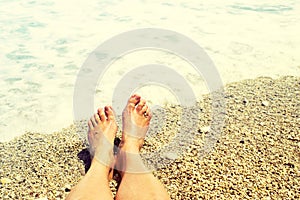 Women`s feet on a pebble beach against the background of sea foam in summer. Beach holidays, holidays, vacation